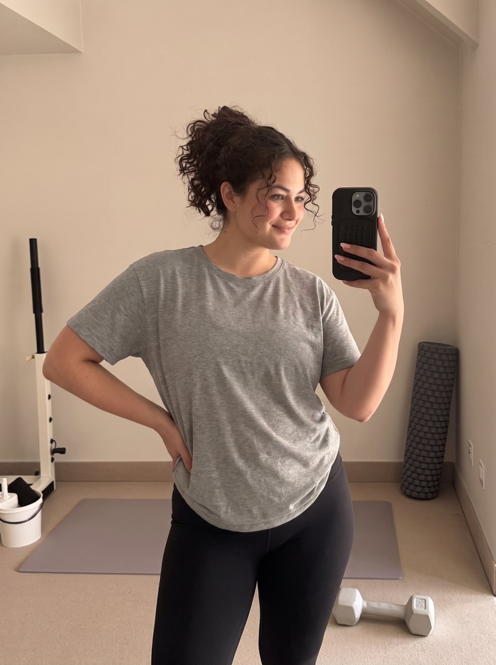 Illustrative: a woman on the first day of strength training, in a grey t-shirt, holding her phone.
